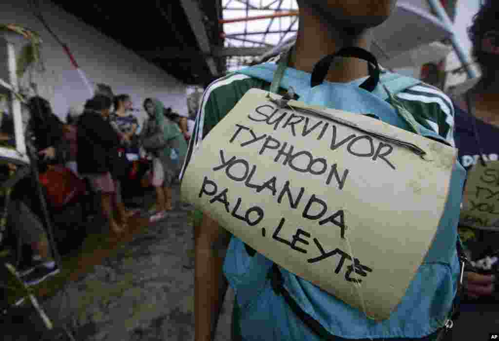 Typhoon survivors hang signs from their necks as they line up to try to board a C-130 military transport plane in Tacloban, Nov. 12, 2013. 