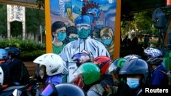 Para pengendara sepeda motor berhenti di dekat mural yang mempromosikan kesadaran akan wabah COVID-19 di Jakarta, 1 Desember 2020. (REUTERS / Ajeng Dinar Ulfiana)
