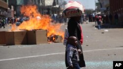 FILE: A woman and child pass a fire set alight during a protest in Harare, Friday, Aug. 26, 2016. (AP Photo)