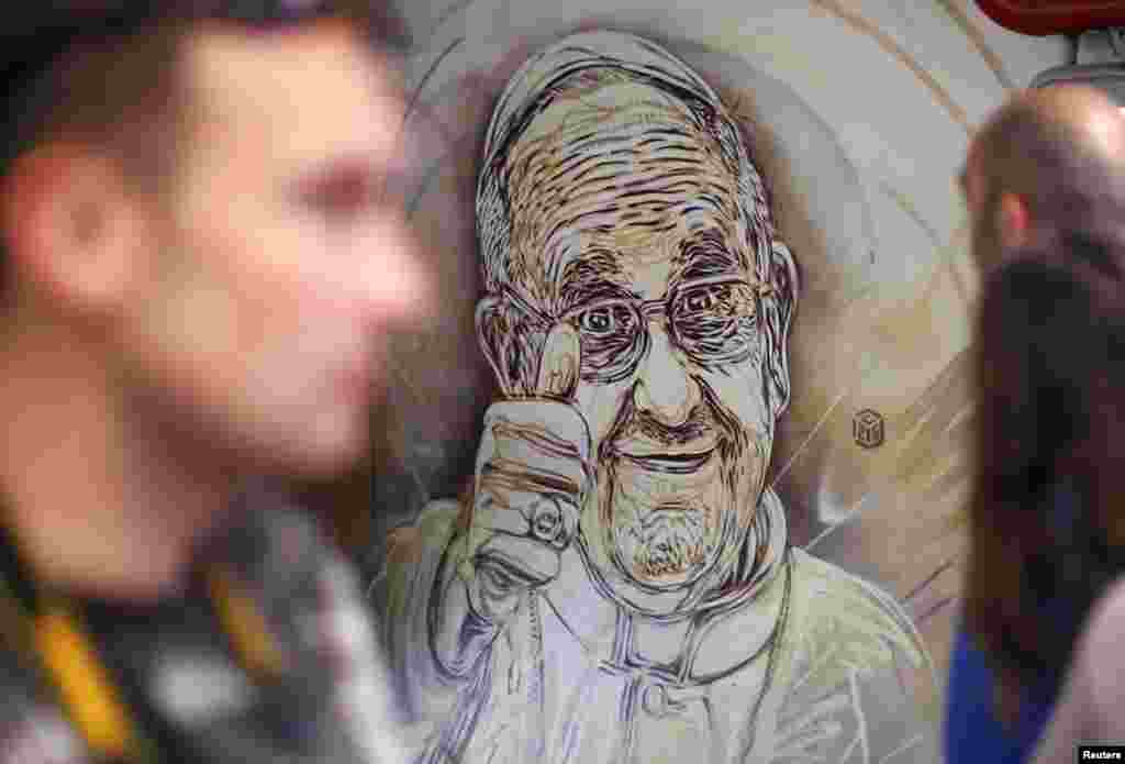 People pass a mural by French street artist Christian Guemy, also known as C215, which depicts Pope Francis giving the thumbs-up sign, in a subway station in Rome. The mural is near a ticket booth at the subway stop at the Spanish Steps, one of the capital&#39;s most popular tourist stops.