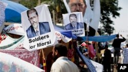 A supporter of Egypt's Islamist President Mohamed Morsi in front pictures of Morsi at Nasr City, where protesters have installed their camp and hold their daily rally, in Cairo, Egypt, July 25, 2013.