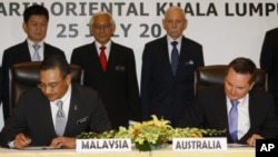 Malaysian Home Minister Hishammuddin Hussein, foreground left, and Australian Immigration Minister Chris Bowen, foreground right, sign documents to swap refugees between the two countries, in Kuala Lumpur, Malaysia, July 25, 2011