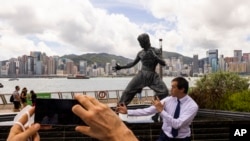 Seorang penggemar menirukan gaya Bruce Lee, di depan patung legenda seni bela diri tersebut dalam rangka memperingati 50 tahun kematiannya di Hong Kong, Kamis, 20 Juli 2023. (AP Photo/Louise Delmotte)