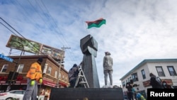 Community members help erect a new fist statue made of steel in the square where George Floyd, a 46-year-old Black man, died after a white police officer knelt on his neck for nearly nine minutes, in Minneapolis, Minn., Jan. 18, 2021.
