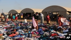 FILE - Displaced Iraqis from the Yazidi community look for clothes to wear among items provided by a charity organization at the Nowruz camp, in Derike, Syria, Aug. 12, 2014.