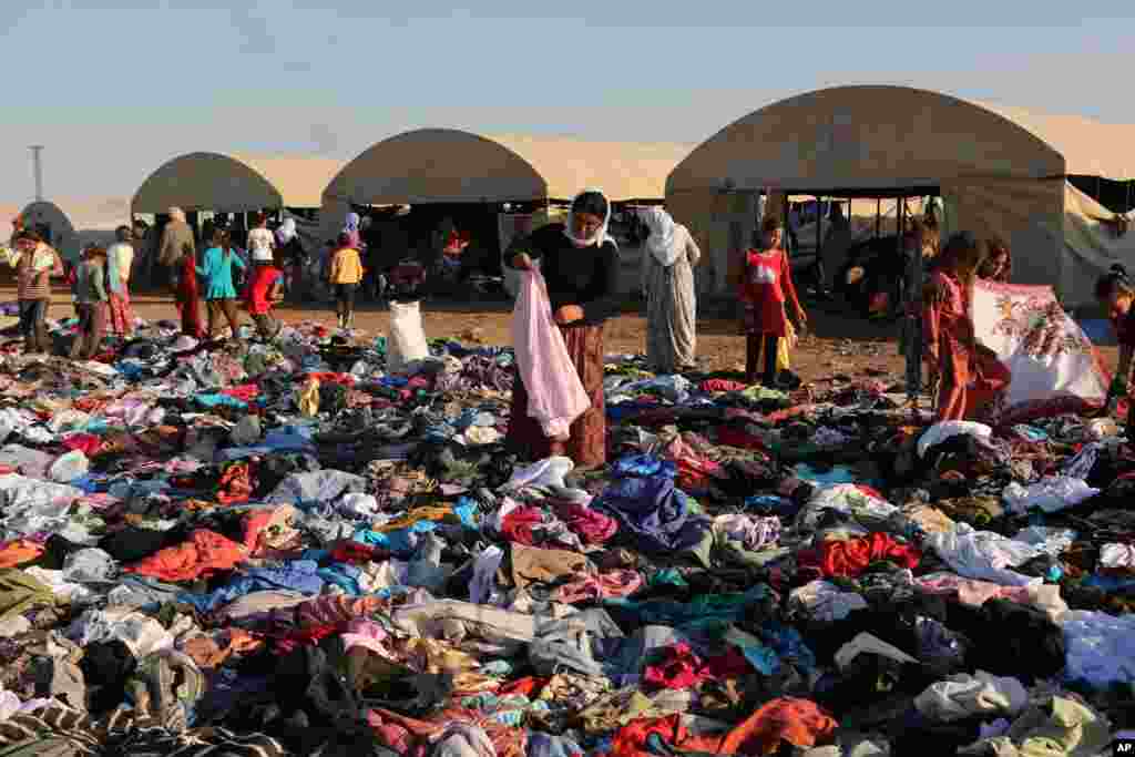 FILE - Displaced Iraqis from the Yazidi community look for clothes to wear among items provided by a charity organization at the Nowruz camp, in Derike, Syria, Aug. 12, 2014.