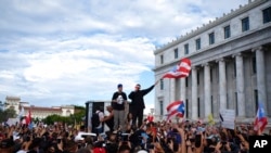 El rapero puertorriqueño René Juan Pérez, conocido como Residente, y Benito Antonio Martínez Ocasio, cuyo nombre artístico es Bad Bunny, animan a manifestantes frente al Capitolio antes de una marcha contra el gobernador Ricardo Rosselló, en San Juan, Puerto Rico.