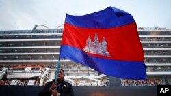 Seorang pria Kamboja memegang bendera nasionalnya di depan MS Westerdam, milik Holland America Line, berlabuh di pelabuhan Sihanoukville, Kamboja, Jumat, 14 Februari 2020. (Foto: AP)