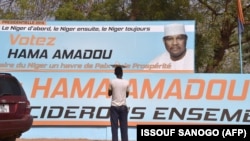 Un homme se tient devant une affiche de campagne du candidat présidentiel Hama Amadou à Niamey le 27 février 2016.