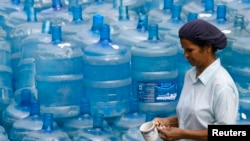 FILE - A woman walks past empty water containers at a water treatment plant in Colombo.