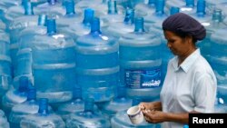 Una mujer pasa frente a recipientes de agua vacíos. La Tierra está cubierta de agua, pero el agua potable es cada vez más escasa.