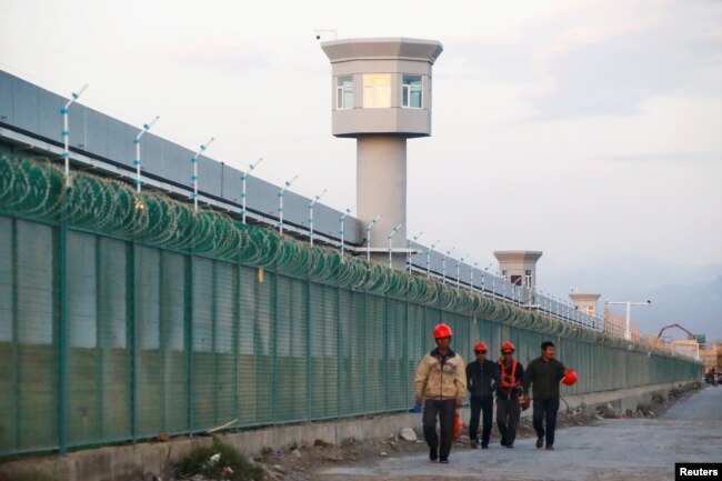 FILE - Workers walk by the perimeter fence of what is officially known as a vocational skills education center in Dabancheng in Xinjiang Uighur Autonomous Region, China, Sept. 4, 2018.