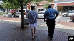 FILE - A woman who voluntarily went to the police for help kicking her heroin addiction walks from the police station for her ride to an area detox facility, in Gloucester, Massachusetts, July 10, 2015.