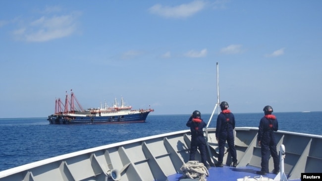 FILE PHOTO: Philippine Coast Guard personnel survey several ships believed to be Chinese militia vessels in Sabina Shoal in the South China Sea, in a handout photo distributed by the Philippine Coast Guard on May 5 and taken according to source on April 2