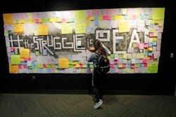 In this November 14, 2019, photo, a student attaches a note to the Resilience Project board on the campus of Utah Valley University, in Orem, Utah. The purpose of the project is to let students know that it is OK to struggle.