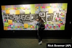 In this November 14, 2019, photo, a student attaches a note to the Resilience Project board on the campus of Utah Valley University, in Orem, Utah. The purpose of the project is to let students know that it is OK to struggle.