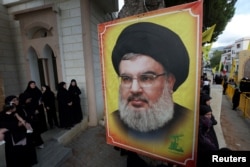 Orang-orang berdiri di dekat foto pemimpin Hizbullah Sayyed Hassan Nasrallah di Kfar Melki, Lebanon, 19 September 2024. (Foto: REUTERS/Aziz Taher)