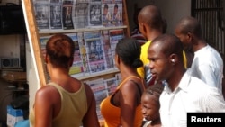 FILE - People read news headlines at a newsstand in Conakry, March 28, 2014. 