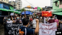 FILE - A man records protesters on his mobile phone as they take part in a demonstration against the military coup, in Yangon, Myanmar, May 21, 2021. 