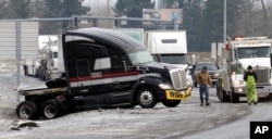 Truck driver Brad Cottle, left, from Florida, surveys the situation with his truck stuck in a ditch with tow truck driver Donny Callahan in Troutdale, Ore., Jan. 18, 2017. An ice storm shut down parts of major highways and interstates Wednesday in Oregon and Washington state.