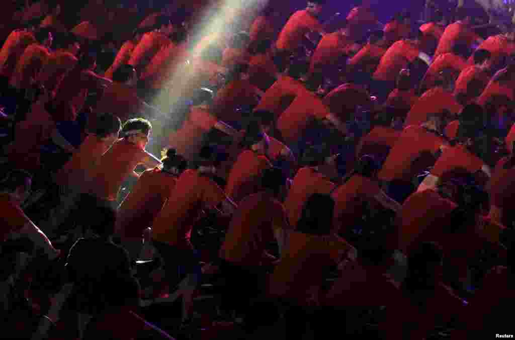 A participant is seen under a beam of light as hundreds of people ride indoor bicycles during a campaign to promote body-building exercises, at a gymnasium in Kunming, Yunnan province, China, Dec. 1, 2015.