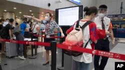 FILE - Airline employees redirect a traveler at a checkpoint for passengers from high-risk areas to present their COVID-19 test results before checking in for their flight at the Beijing Capital Airport terminal 2 in Beijing on Wednesday, June 17, 2020.