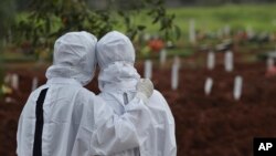 Des membres de la famille regardent des ouvriers enterrer un cercueil dans la section spéciale du cimetière de Padurenan qui a été ouverte pour faire face à l'augmentation des décès dû à l'épidémie de coronavirus à Bekasi, en Indonésie, jeudi 17 juin 2021.