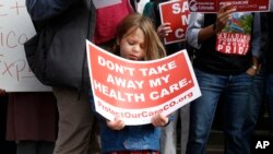 FILE - A girl stands holding a sign alongside supporters of the Affordable Care Act who are also opponents of Colorado's GOP-led plan to undo Colorado's state-run insurance exchange at a rally on the state Capitol steps in Denver, Jan. 31, 2017. 