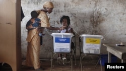 A woman carrying a baby on her back votes at a polling station in Freetown on November 17, 2012. 