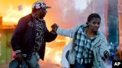 A couple run past burning shops during clashes in Nairobi, Kenya, Oct. 27, 2017.