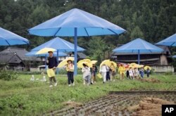 FILE - Public school students carry their own yellow umbrellas through a rice paddy dotted with giant blue umbrellas from the project by Christo in Japan's Sato River Valley, Oct. 9, 1991. (AP Photo/Mitsuhiko Sato)