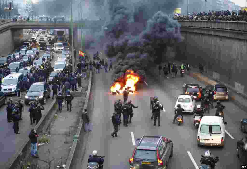 Polisi anti huru-hara tiba ketika pengemudi taksi memblokir jalan dengan membakar ban saat unjuk rasa menentang layanan transportasi VTC seperti Uber, di jalan lingkar di porte Maillot di Paris, Perancis.