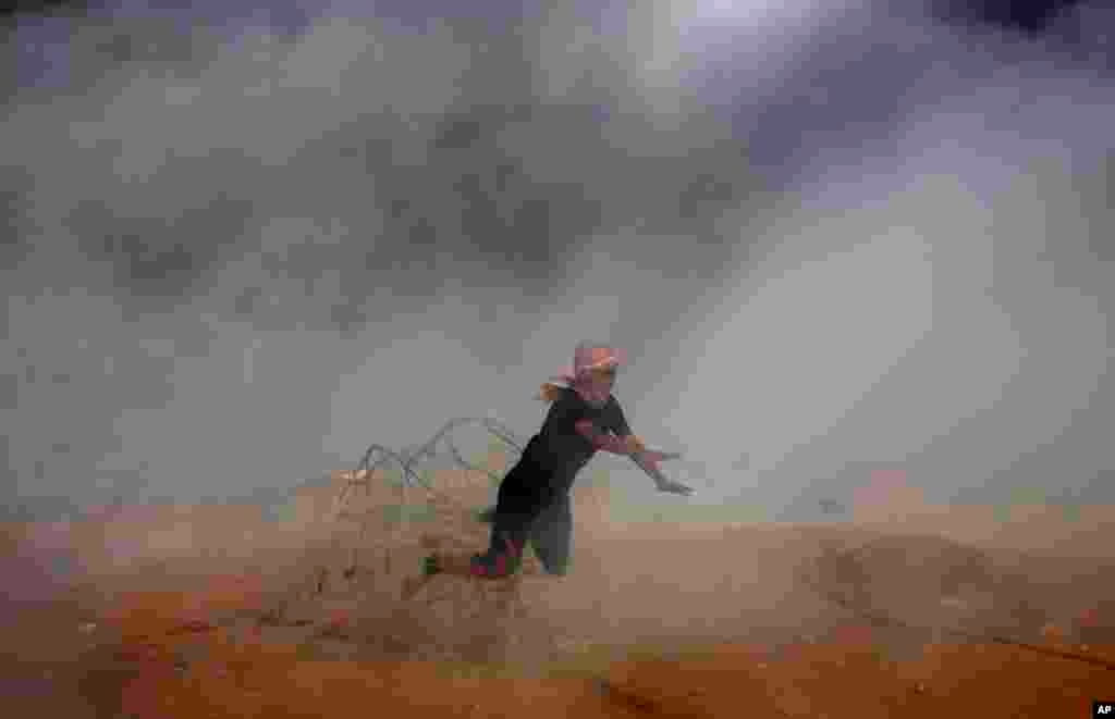 A protester falls down on barbed fence as he runs for cover from teargas fired by Israeli troops while others burn tires near fence of Gaza Strip border with Israel during a protest east of Khan Younis, southern Gaza Strip.