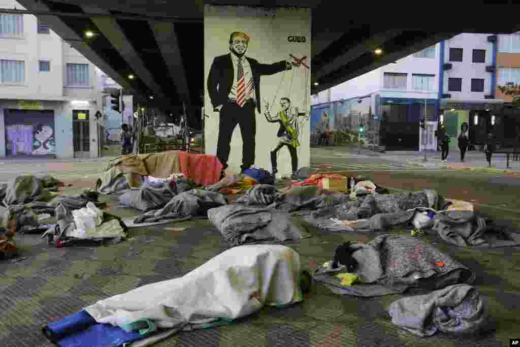 Homeless people sleep under a bridge in front of a mural depicting US President Donald Trump as a puppeteer manipulating Brazil&#39;s President Jair Bolsonaro, in downtown Sao Paulo, Brazil.