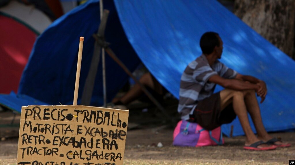 En esta foto del 11 de marzo del 2018, un cartel que dice 'necesito trabajo. Conductor de tractores. Excavador', cerca a un migrante venezolano que descansa fuera de su tienda de camapaña en la plaza Simón Bolívar, donde los venezolanos se han instalado en Boa Vista, Roraima, Brasil.