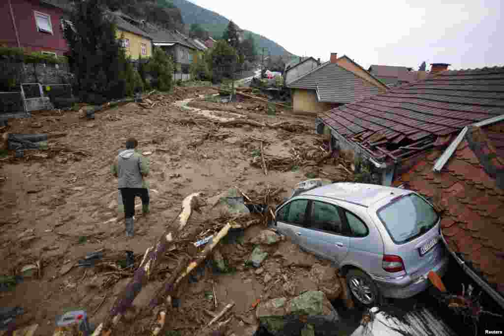 Một người đàn ông đi ngang qua một chiếc xe bị hư hại trên một con đường ngập bùn do lũ lụt nặng nề ở làng Tekija, Serbia. 