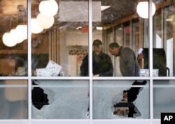 People look over the area near a window shot out at a Waffle House restaurant, April 22, 2018, in Nashville, Tenn. At least four people died after a gunman opened fire at the restaurant early Sunday.