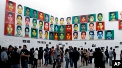 People stand under the portraits of 43 college students who went missing in 2014 in an apparent massacre, by Chinese concept artist and government critic Ai Weiwei at the Contemporary Art University Museum in Mexico City, Mexico, April 13, 2019.