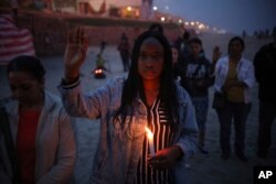 FILE - A woman holding a candle observes a minute of silence in memory of migrants who have died during their journey toward the U.S., near the border fence that separates Mexico from the U.S., in Tijuana, Mexico, June 29, 2019.