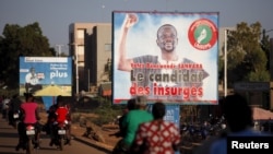 People ride motorcycles past a billboard for presidential candidate Benewende Sankara in Ouagadougou, Burkina Faso, Nov. 28, 2015. The billboard reads, "Vote Benewende Sankara, the insurgents' candidate."