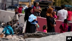 People carry their luggage as they cross into Syria on foot, through a crater caused by Israeli airstrikes aiming to block Beirut-Damascus highway at the Masnaa crossing, in the eastern Bekaa Valley, Lebanon, Oct. 5, 2024.