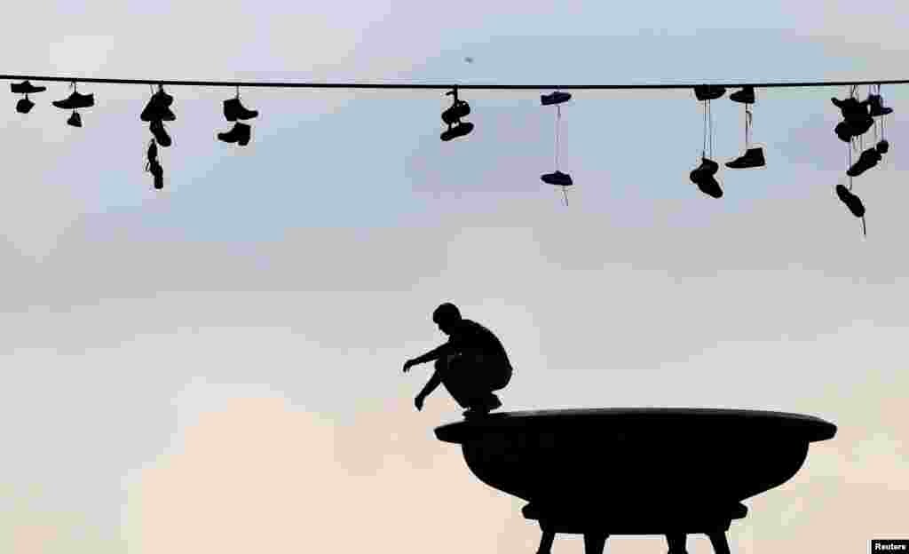 Shoes hang from a power line as a man balances on a statue in a park in Prague, Czech Republic.