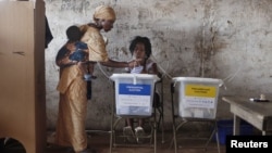 A woman carrying a baby on her back votes in Freetown, Sierra Leone Nov. 17, 2012. 