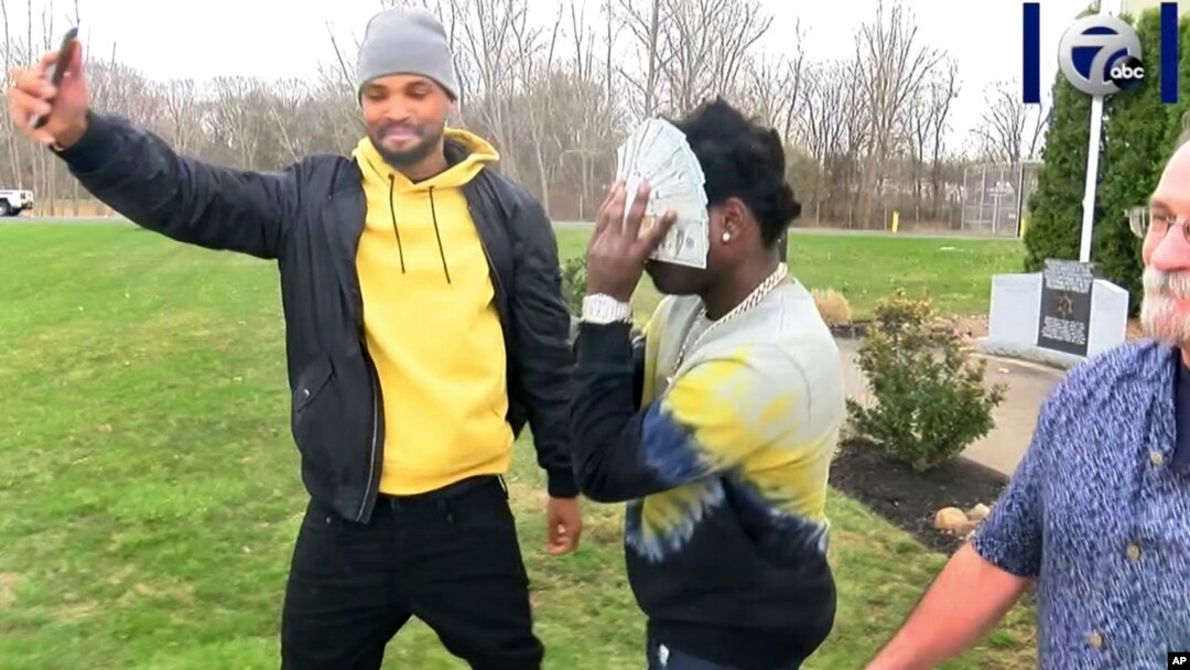 Bill Kapri, center, also known as rapper Kodak Black, covers his face with $100 bills as he walks out of jail after making bail, April 18, 2019 in Lewiston, N.Y.