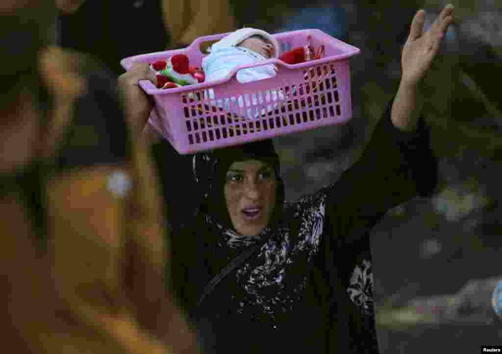 An Iraqi Sunni displaced woman, carrying her child, flees the violence in the city of Ramadi, May 19, 2015. Iraqi security forces deployed tanks and artillery around Ramadi to confront Islamic State fighters who have captured the city in a major defeat for the Baghdad government and its Western backers.