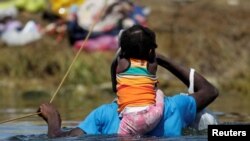 Seorang migran menggendong anaknya ketika menyebrangi sungai Rio Grande di perbatasan AS-Meksiko untuk mencari suaka di wilayah Amerika Serikat pada 22 September 2021. (Foto: Reuters/Daniel Becerril)