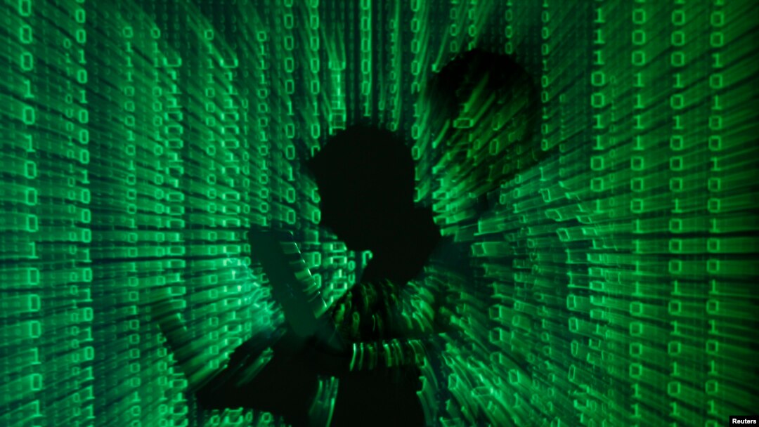 Illustration shows projection of binary code on a man holding a laptop computer, in an office.