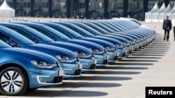 People walk past a row of Volkswagen e-Golf cars during the company's annual news conference in Berlin March 13, 2014.