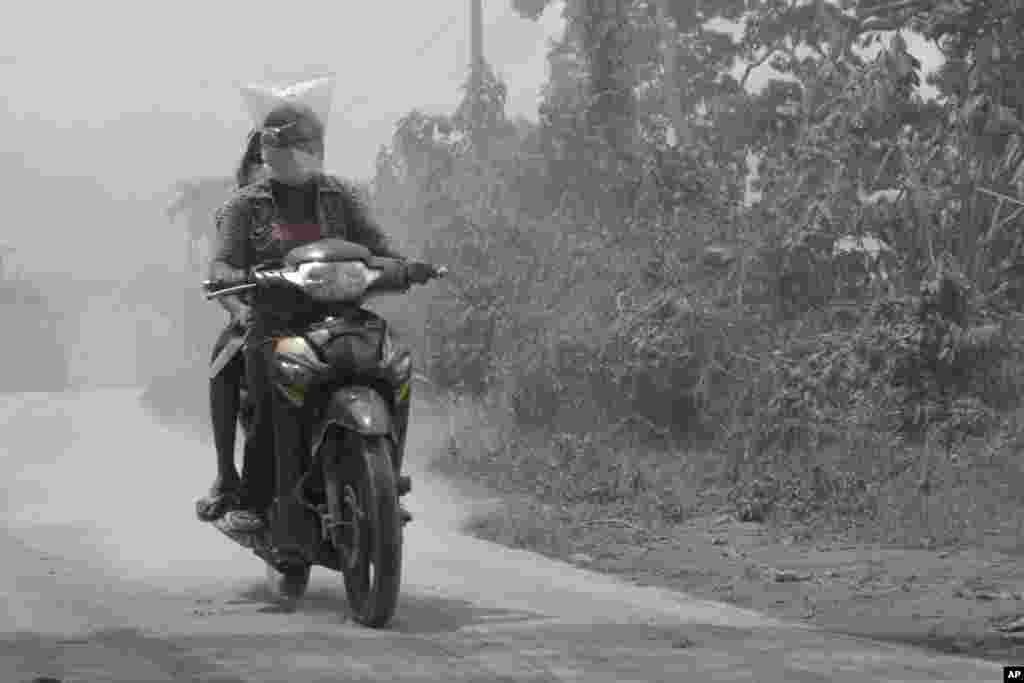 Warga mengendarai sepeda motor dengan kepala ditutup plastik, di jalanan yang diselimuti abu vulkanik dari letusan Gunung Sinabung di Kuta Mbaru, Sumatera Utara. (AP/Mafa Yuli Ramadani)