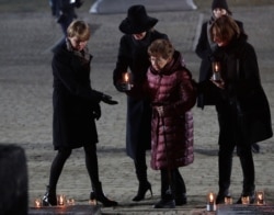 Holocaust survivor Bat-Sheva Dagan, center, is escorted as she is about to put a candle at the Auschwitz Nazi death camp in Oswiecim, Poland, Jan. 27, 2020.